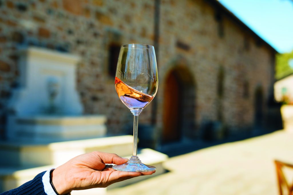 a hand holding a glass of rosé wine in front of a rock building