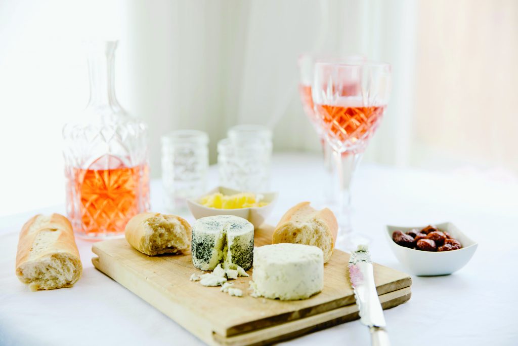 glass of rosé wine sitting on a counter with cheeses
